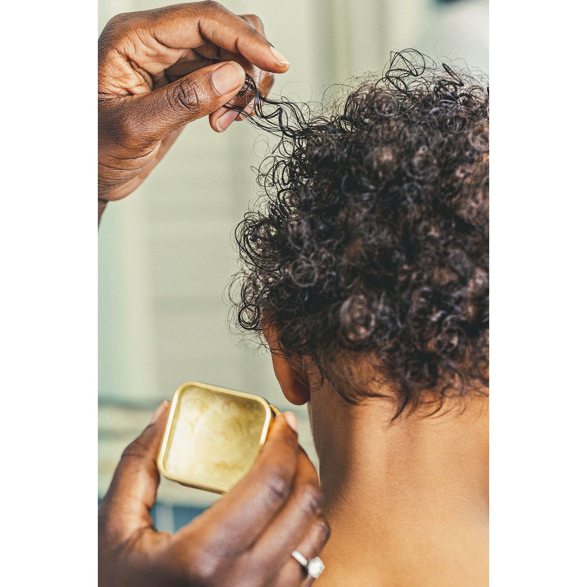 Shea butter being applied to the curly hair of a child for hair care and moisture
