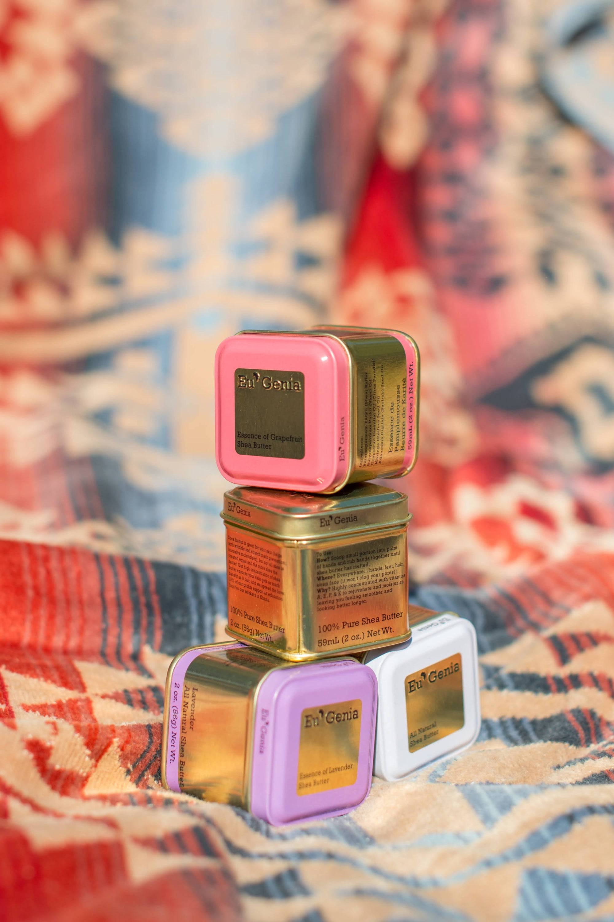 Four tins of Eu'Genia from the moisturizing gift bundle are stacked on a colorful background