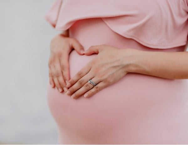 Pregnant woman in a pink dress with her hands on her belly in the shape of a heart