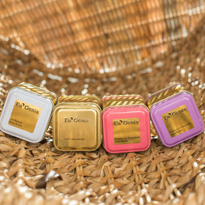 Four tins in white, gold, pink, and purple(from left to right), in a row in a basket with light shining through.