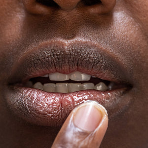 Close up image of lips with one finger applying shea butter to the lips.